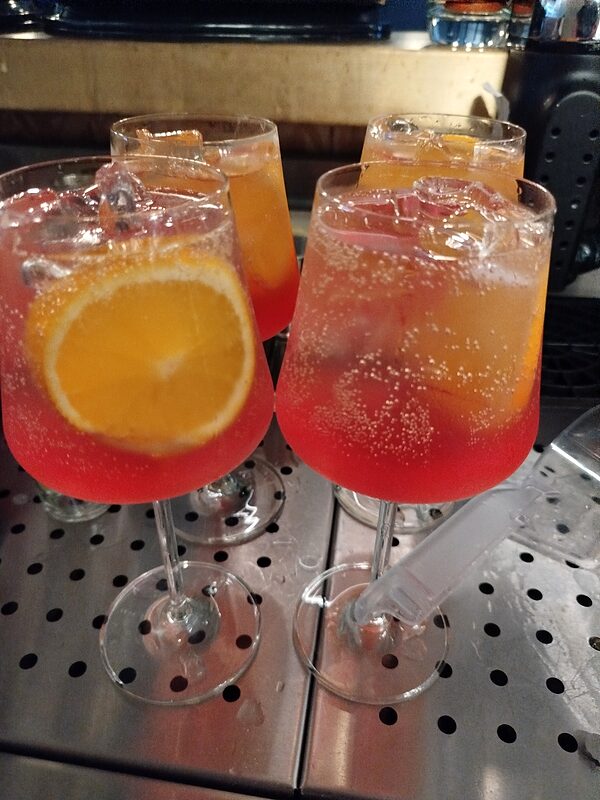 Three spritzes with orange slices on a steel bar tray, just made
